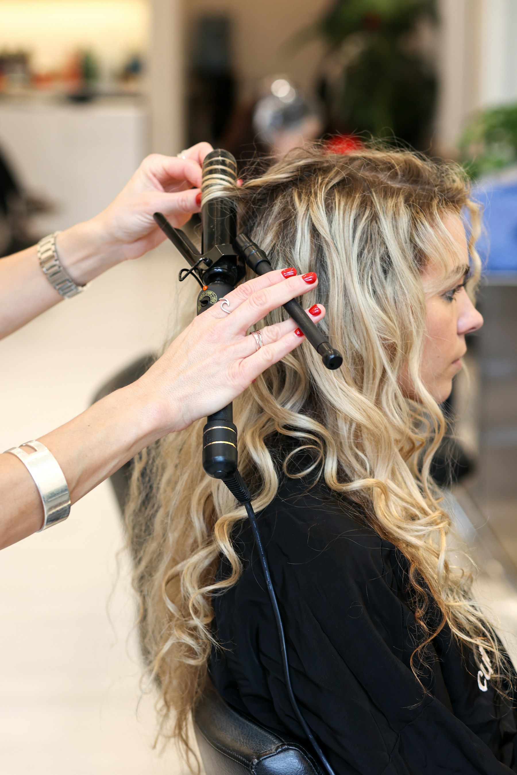A hairstylist using a curling iron to style a client's hair in a salon